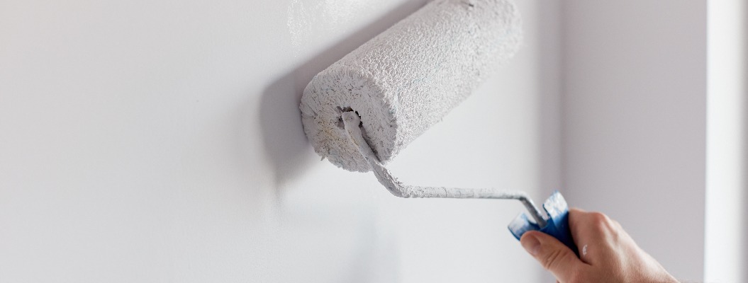 Male hand painting wall with paint roller. Painting apartment, renovating with white color paint