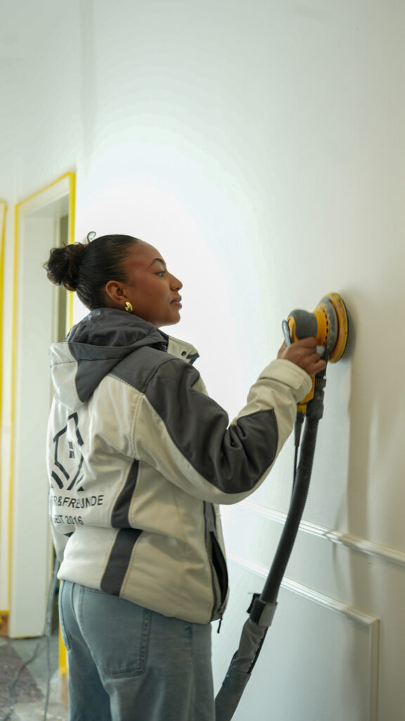 Mitarbeiterin schleift eine Wand, die gestrichen werden soll, ab